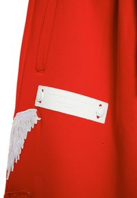 Prenda roja con un acabado texturizado, que presenta una etiqueta blanca con texto en relieve y un detalle decorativo de bordado de alas blancas.