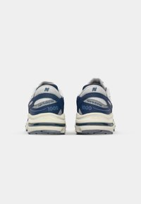 Pár modro-bílých tenisek New Balance 1000 zobrazených zezadu, zdůrazňující síťové panely a polstrované podrážky.