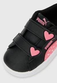 Μαύρο παιδικό αθλητικό παπούτσι με ροζ καρδιές ως κούμπωμα, ροζ πλαϊνή επιφάνεια με μικρές καρδιές και ροζ λογότυπο Puma στη γλώσσα και στο πλάι.