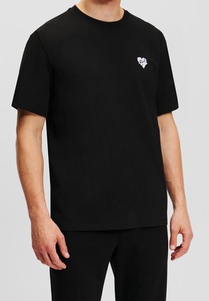 Zwart katoenen T-shirt met korte mouwen, ronde hals en een kleine witte afbeelding op de linkerborst. Soepele, matte textuur.