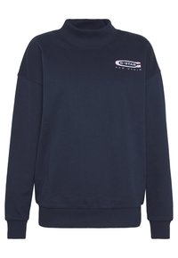 Marinblå sweatshirt med hög krage och långa ärmar, med en logotyp på bröstet. Tillverkad av mjukt material med ribbade muddar och fåll.