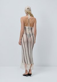 Robe maxi au crochet en crème et marron foncé avec un design ajouré. Dotée d'un col halter, d'un lien dans le dos et d'un ourlet à franges. Texture lisse et légère.