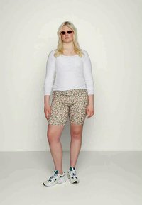 Top de manga longa branco e calções com padrão floral em rosa e verde. Modelo a usar óculos de sol cor de rosa e ténis brancos. Fundo neutro.