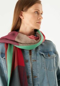 Multikleurige sjaal met schakeringen van rood, groen en beige. Gemaakt van zachte stof met een gestructureerde afwerking, draped om de nek van het model.