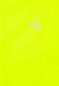Neon gele stof met een gladde textuur heeft een wit "cK" logo. Eenvoudig ontwerp met een contrasterende stiksel detail.