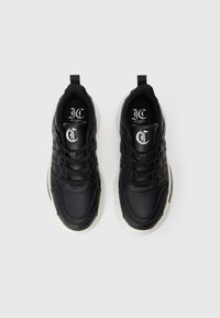 Černé tenisky s bílou podrážkou, složitý design prošití, tkaničky uvázané, a logo 'JC Just Cavalli Milano' uvnitř boty, pohled shora.