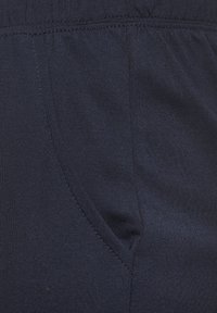 Dunkelblauer Stoff mit glatter Textur, versehen mit einer Seitentasche und einem elastischen Bund. Nahaufnahme, die die Nähdetails hervorhebt.