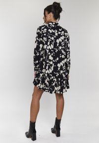 Abito nero con stampa floreale bianca, maniche lunghe, orlo arricciato e chiusura con bottoni sul retro. Indossato con stivali neri alla caviglia.