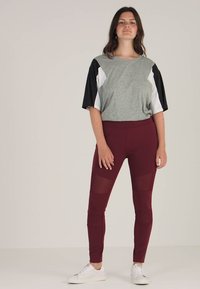 Szürke, rövid ujjú felső, fekete és fehér részletekkel, bordó leggings-szel, hálós panelek kíséretében. Fehér sportcipő egészíti ki az öltözéket.