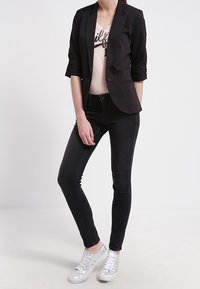 Černý přizpůsobený blazer s ohrnutými rukávy, spárovaný se světle růžovým tričkem s grafikou a černými skinny džíny, doplněný stříbrnými teniskami.