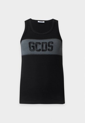 Γυναίκα με μαύρο αμάνικο τοπ με λογότυπο GCDS, σκούρο κόκκινο δερμάτινο παντελόνι, μαύρα μυτερά φλατ παπούτσια και σκουρόχρωμα γυαλιά ηλίου, στέκεται μπροστά σε λευκό φόντο.