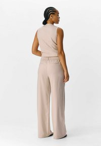 Beige geripptes ärmelloses Top mit hohem Kragen, kombiniert mit lockeren, elastischen weit geschnittenen Hosen. Sanfte Textur und minimalistische Designmerkmale.