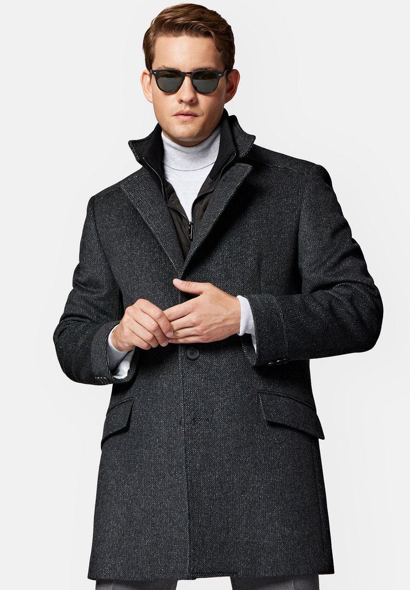 Ciemnoszara kurtka wełniana z klapami, z zamknięciem na guziki z przodu oraz dwoma bocznymi kieszeniami. Nosi się ją na jasnym golfie i zestawia z okularami przeciwsłonecznymi.