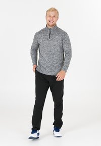 Lätt grå melange zip-up-tröja med långa ärmar och hög krage, ihop med svarta byxor och vita sneakers med blå accenter.