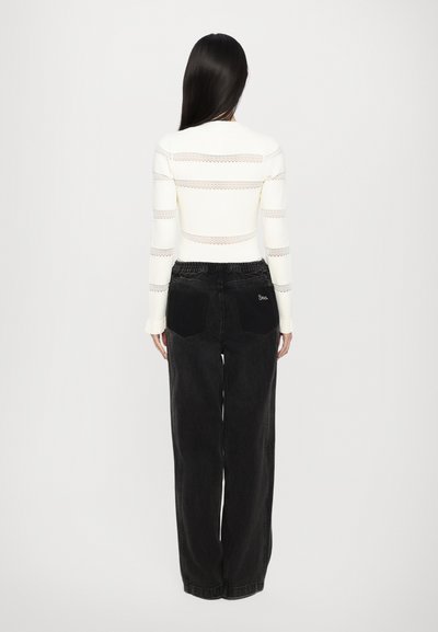 White knitted top with horizontal lace stripes, paired with black wide-leg jeans featuring two back pockets and a logo detail.