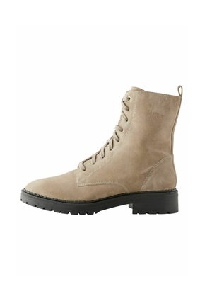 Bottines en suède beige avec un bout rond, un laçage à l'avant et une semelle en caoutchouc noire. Présente des détails de couture et une languette à l'arrière.