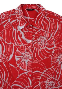 Chemise rouge à boutons avec un motif floral abstrait blanc et un col pointu, taille petite avec une étiquette de marque visible "CALLIOPE."