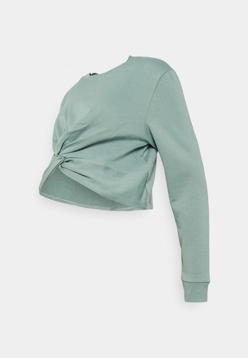 Chemise courte à manches longues vert clair avec un détail de nœud torsadé à l’avant, présentée sur un fond uni.