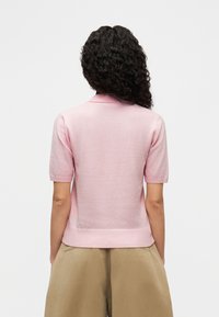 Ροζ ανοιχτό ροζ πλεκτό πόλο με κοντά μανίκια, με ριμπ τελείωμα και μαλακή υφή. Απλός σχεδιασμός χωρίς επιπλέον σχέδια ή διακοσμήσεις.