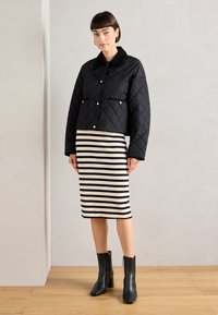 Black quilted jacket with a collar, two front pockets, paired with a black and white striped pencil skirt and black heeled ankle boots.