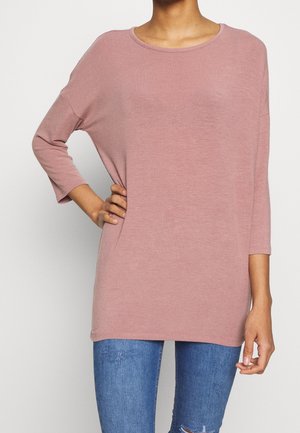 Lichtroze langemouwen top met een ronde halslijn, een losse pasvorm en een zachte textuur. Gecombineerd met blauwe denim jeans met een lichte slijtage.
