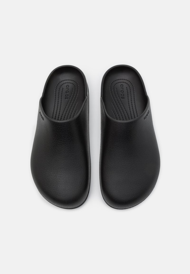 Zapatos negros sin cordones, hechos de un material suave, con una forma redondeada, diseño minimalista y una marca grabada en el lateral.