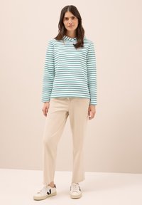 Camiseta de manga larga a rayas de color azul claro con capucha y rayas horizontales de color verde oscuro, combinada con pantalones rectos beiges y zapatillas blancas.