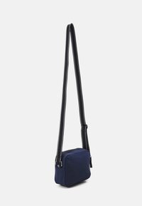 Piccola borsa a tracolla blu navy con cintura regolabile nera, caratterizzata da cuciture bianche e una chiusura con zip superiore.