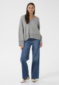 Pulover gri tricotat cu decolteu în V și umeri căzuți, purtat cu blugi blue denim evazați și pantofi de culoare deschisă.