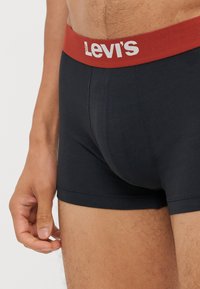 Fekete boxer alsónadrág, piros derékgumival, rajta a fehér "Levi's" logóval. Simább anyag, amely szoros illeszkedést biztosít és erősített varrás részletekkel rendelkezik.