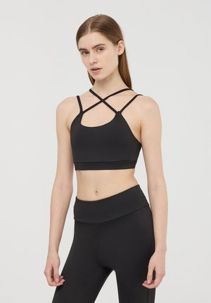 Bralette sportivo nero con spalline incrociate, un'apertura rotonda e un design liscio e aderente. Abbinato a leggings neri a vita alta.