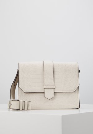 Crèmekleurige crossbodytas van leer met krokodillenstructuur, voorflap en verstelbare gesp, liggend op een wit oppervlak.