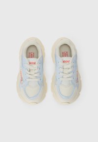 Sneakers med nettingoverdel i myk blå og kremfarge, med lisser, polstret beige såler og rød merkevare på siden.