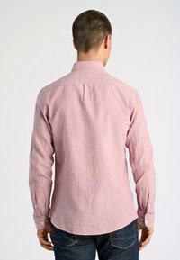 Langemouwen, roze linnen shirt met een kraag, knoopmanchetten en een plooi aan de achterkant. De stof heeft een gestructureerde weving, waardoor een subtiel patroon ontstaat.