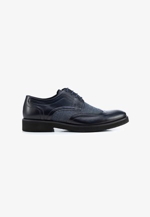 Marineblauwe leren veterschoen met een textuur van blauw stof. Beschikt over een ronde neus, platte zwarte zool en subtiele stiksels.