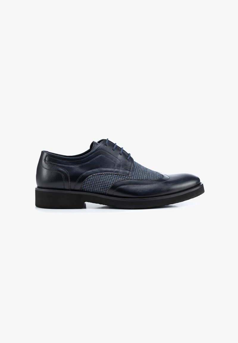 Chaussure en cuir bleu marine à lacets avec un panneau en tissu texturé bleu. Présente un bout arrondi, une semelle noire plate et des détails de couture subtils.