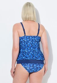 Haut de maillot de bain bleu à motifs avec des bretelles spaghetti, présentant des motifs de feuilles. Assorti à un bas de bikini bleu, le tout en tissu extensible.