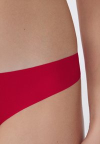 Rote Bikiniunterteile aus einem glatten, elastischen Stoff mit einem minimalistischen Design und dünnem Bund, die eine saubere, moderne Silhouette präsentieren.