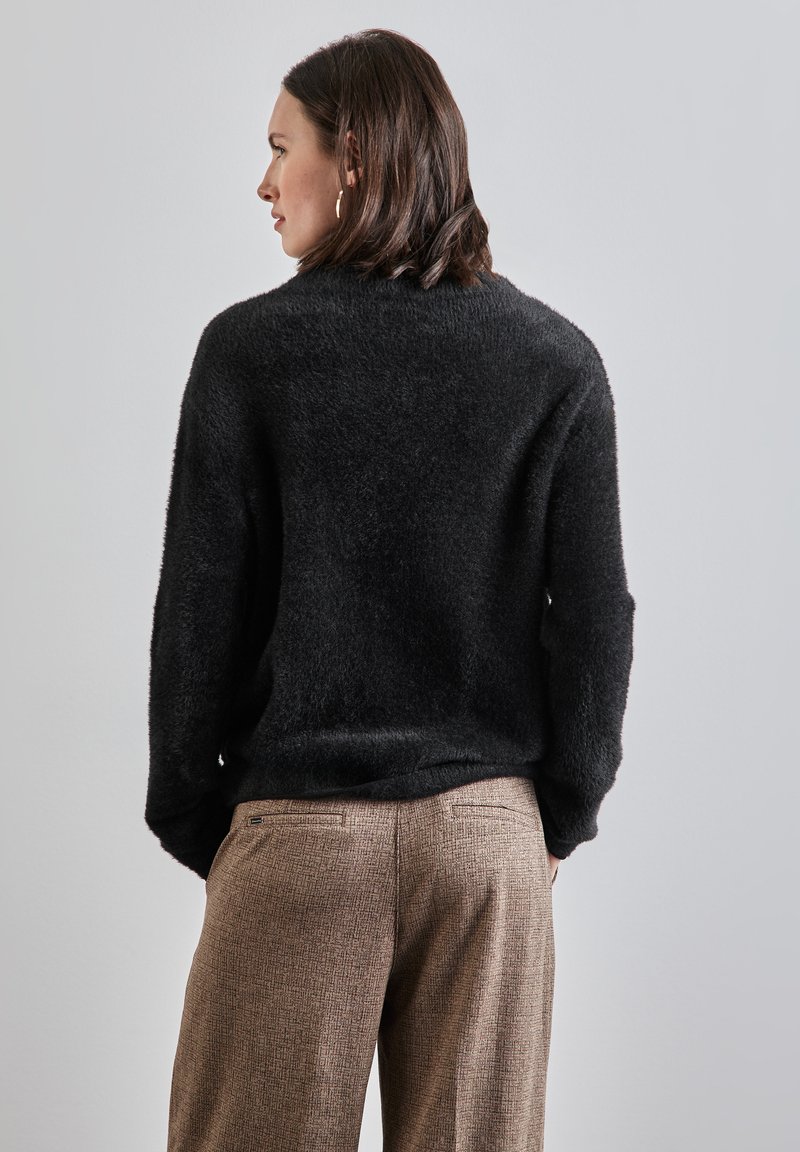 Pull noir en peluche avec une coupe décontractée, assorti à un pantalon texturé marron. La tenue présente un minimum de détails et un look décontracté.