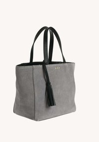 Sac fourre-tout en suedine grise avec poignées en cuir noir et détail de pampille, comportant trois petits points dorés près du bord supérieur.