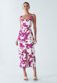 Robe midi fleurie blanche avec des motifs violets audacieux, encolure carrée, larges bretelles et fente frontale ; confectionnée en tissu léger.