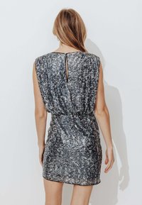 Robe métallisée argentée avec un design texturé et côtelé. Présente des manches courtes, une silhouette ajustée et une petite ouverture en forme de clé au dos.