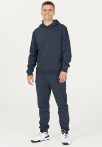 Marinblå hoodie och matchande joggers tillverkade av mjukt tyg, med en avslappnad passform, ribbade ärmslut och en diskret logotyp på bröstet.