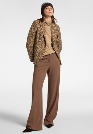Leopardenmuster-Blazer in Braun und Tan, kombiniert mit einem beigen Rollkragenpullover und braunen weiten Hosen. Wollstrickmütze in Dunkelbraun.