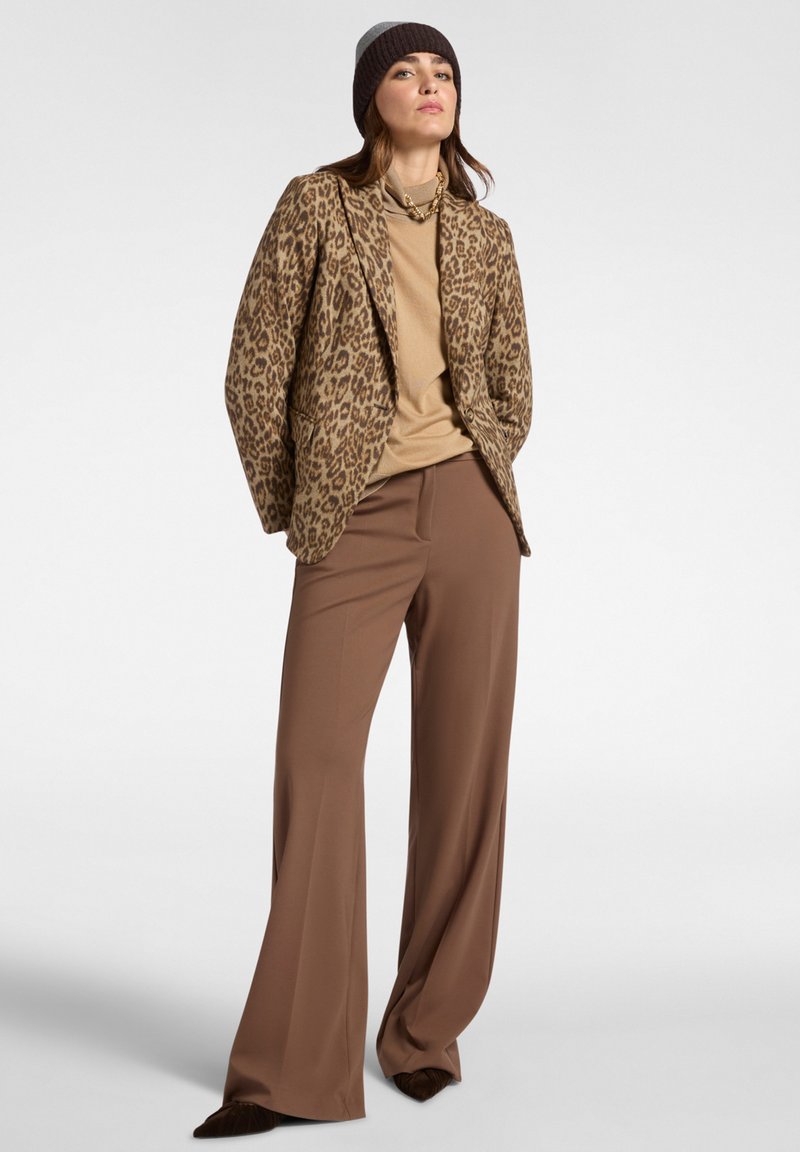Blazer leopard in tonalità marrone e tan, abbinato a un dolcevita beige e pantaloni palazzo marroni. Cappello in maglia di lana di colore marrone scuro.