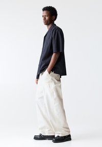 Short-sleeve navy shirt with a pocket, paired with loose-fitting beige pants. Black shoes with a chunky sole complete the outfit.