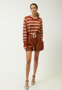 Rostfarbenes und creme gestreiftes Strickpullover mit entspanntem Schnitt. Braune Leder-Shorts mit hoher Taille und breitem Gürtel mit Strassschnalle. Glitzernde Absätze.