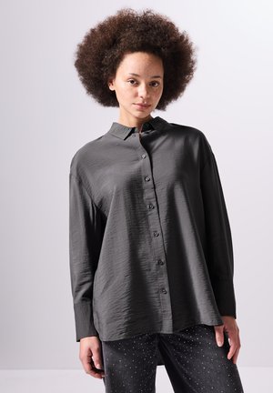 Dark gray button-up shirt with a textured finish, long sleeves, and a collar. Paired with dark jeans featuring metallic accents.