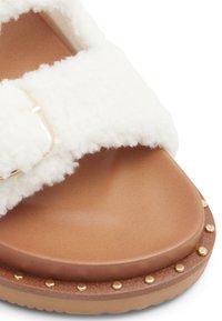 Hvide fluffy strap-sandaler med en brun formet fodseng og en guldbuckle-accent. Sålens kant har en detaljeret kant med guldnitter.