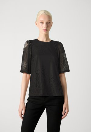 Haut noir avec de courtes manches bouffantes en dentelle, arborant un design à motifs floraux et une texture de tissu lisse, associé à un pantalon noir.